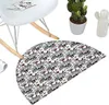 A close-up view of a rug with a skull pattern, placed on the floor near a white rocking chair. A potted cactus and a white ceramic cactus figurine are visible in the background. Voir les images du produit