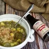 A bowl of green stew with potatoes and meat, next to a bottle of Worcestershire sauce. Produktbild-Vorschau