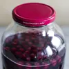 A close-up shot of a glass jar filled with red cherries and liquid, with a red lid. Produktbild-Vorschau