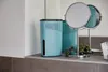A turquoise dehumidifier sits on a bathroom counter next to a double-sided mirror and some greenery. Produktbild-Vorschau