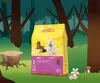 A bag of dog food is displayed in a cartoon forest setting with a tree stump and mushrooms. Produktbild-Vorschau