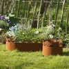 Two metal garden borders with decorative cutouts are placed on a grassy lawn in front of a wooden fence and flowering plants. Produktbild-Vorschau