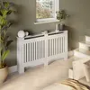 A white radiator cover is placed in a room with a plant and a window. Náhled obrázku produktu