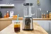 A blender and a glass of juice on a wooden countertop in a kitchen. Podgląd zdjęcia produktu