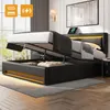 A modern black upholstered bed with its storage compartment open, revealing stored items. The bed features integrated LED lighting along the headboard and base. Produktbild-Vorschau