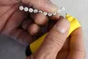 Hands holding a string of white beads and a yellow tool. Produktbild-Vorschau