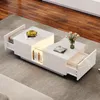 A modern white coffee table with drawers and integrated lighting is placed on a gray rug in a living room setting, with a wooden floor in the background. Produktbild-Vorschau