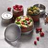 Three glass lunch containers filled with food, along with some loose strawberries and tomatoes, are arranged on a textured gray surface. Podgląd zdjęcia produktu