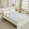 Weiße gesteppte Matratzenauflage mit elastischen Bändern auf einem weißen Bett mit zwei Kissen in einem hellen Schlafzimmer Náhled obrázku produktu