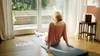 A woman is sitting on a yoga mat in a room, looking out a large window at a garden. The word "HOLIDAY" is visible on the window, and the word "HOME" is visible on the floor. Anteprima dell’immagine prodotto