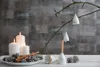 A festive Christmas arrangement with lit candles, pinecones, cinnamon sticks, and hanging porcelain bells on a branch. Produktbild-Vorschau