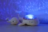 Two plush whale toys are shown in a dimly lit room with blue light projected onto the wall behind them, creating a water-like effect. Anteprima dell’immagine prodotto