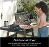 A woman is using an outdoor air fryer on a patio. Voir les images du produit