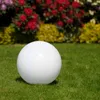 A white sphere sits on a green lawn in front of a blurred background of red and yellow flowers. Produktbild-Vorschau