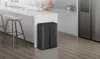 A modern kitchen scene with a person preparing food at a counter and a black recycling bin in the foreground. Produktbild-Vorschau