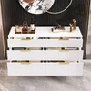 A modern white sideboard with gold handles, drawers partially open, displaying decorative items and bottles on top. Podgląd zdjęcia produktu