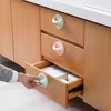 A hand is pulling open a drawer on a wooden cabinet. The drawer has a light green handle. The cabinet has two other drawers with light green and pink handles. Produktbild-Vorschau