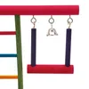 A close-up view of a colorful bird toy, featuring a swing with purple bars and a red seat, suspended from a red bar. A silver bell hangs from the center. Náhled obrázku produktu