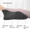 A person's legs are resting on a black wedge-shaped cushion, with labels indicating different support areas. Produktbild-Vorschau