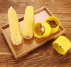 Two ears of corn and three yellow corn peelers are arranged on a wooden tray. Produktbild-Vorschau