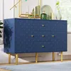 A navy blue dresser with gold legs and gold drawer pulls, decorated with a scalloped pattern. It is placed on a light blue rug in a well-lit room. Voir les images du produit