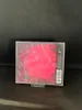 A CD case with a red and black abstract design, encased in plastic wrap, is displayed on a black surface. Produktbild-Vorschau