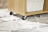 A close-up shot of the bottom of a wooden cabinet with wheels, resting on a patterned rug. Podgląd zdjęcia produktu