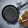 A frying pan is shown on a gray surface with some ingredients and a cutting board. Produktbild-Vorschau