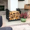 A black metal firewood rack filled with logs is placed next to a potted plant in a living room setting. Náhľad obrázku produktu
