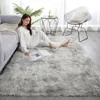 A woman in pajamas sits on a fluffy gray rug reading a book, next to a sofa and a modern chair. Podgląd zdjęcia produktu