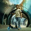 A young boy stands on a scooter in a tunnel with aquarium-like walls. Voir les images du produit