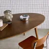 A close-up shot of a wooden oval dining table with decorative items and a chair. Produktbild-Vorschau