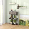 A plant stand with plants and decorative items in a room with a window and a painting. Produktbild-Vorschau
