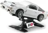 A white Lego-style model of a Mazda FC3S RX-7 car is displayed on a black stand, simulating a car lift. The car is angled upwards, showcasing its front and side. Produktbild-Vorschau