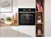 A modern kitchen scene featuring a built-in oven and a shelving unit with decorative items and books. Produktbild-Vorschau