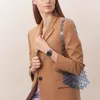 A woman wearing a brown blazer and a silver watch, holding a blue beaded bag. Voir les images du produit
