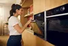 A woman is opening the door of a built-in oven in a modern kitchen. Produktbild-Vorschau