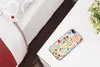 A phone case with a floral pattern is placed on a white nightstand next to a bed. Produktbild-Vorschau