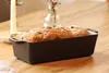 A loaf of bread in a black cast iron baking pan sits on a wooden table. Produktbild-Vorschau