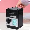 A hand is inserting a coin into a black electronic piggy bank safe with a keypad and a dial. Náhled obrázku produktu
