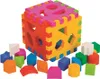 A colorful shape-sorting cube toy with various geometric shapes scattered around it. Anteprima dell’immagine prodotto