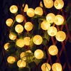A string of solar-powered lantern lights are strung along a wooden fence with green foliage. Produktbild-Vorschau
