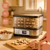A food dehydrator filled with dried mushrooms, with fresh mushrooms and a knife on a cutting board in the foreground. Náhled obrázku produktu