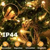 Close-up of warm white LED string lights on a green, possibly Christmas tree, background with rain effects. Text and icons indicating weather resistance are present. Produktbild-Vorschau