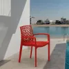 A red chair is placed on a patio next to a pool, with a body of water and buildings in the background. Produktbild-Vorschau