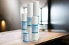 Several white cylindrical water filters of varying heights are arranged on a wooden table in front of a blurred background. Produktbild-Vorschau