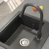 A close-up view of a black granite kitchen sink with a black faucet and a silver drain. Náhled obrázku produktu