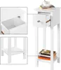 A white wooden nightstand with a drawer and two shelves, shown with a cup and books on top and one shelf. Produktbild-Vorschau