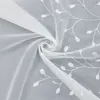A close-up view of white sheer fabric with embroidered leaf patterns, swirled to show texture and detail. Produktbild-Vorschau