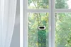 A window cleaning robot is attached to a window, with trees and sunlight visible through the glass. Produktbild-Vorschau